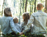 A family of 4 sitting in the forest floor, looking out to the trees in front.