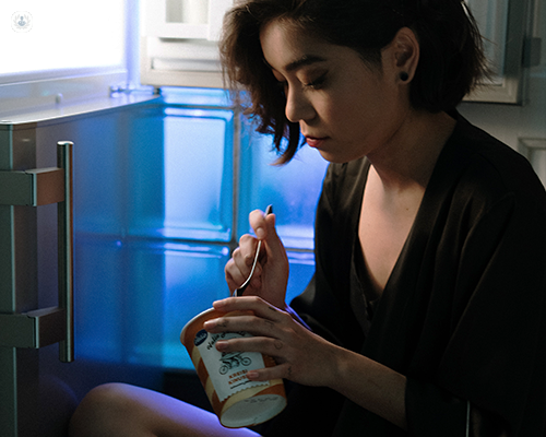 A woman sat by the fridge binging on ice cream
